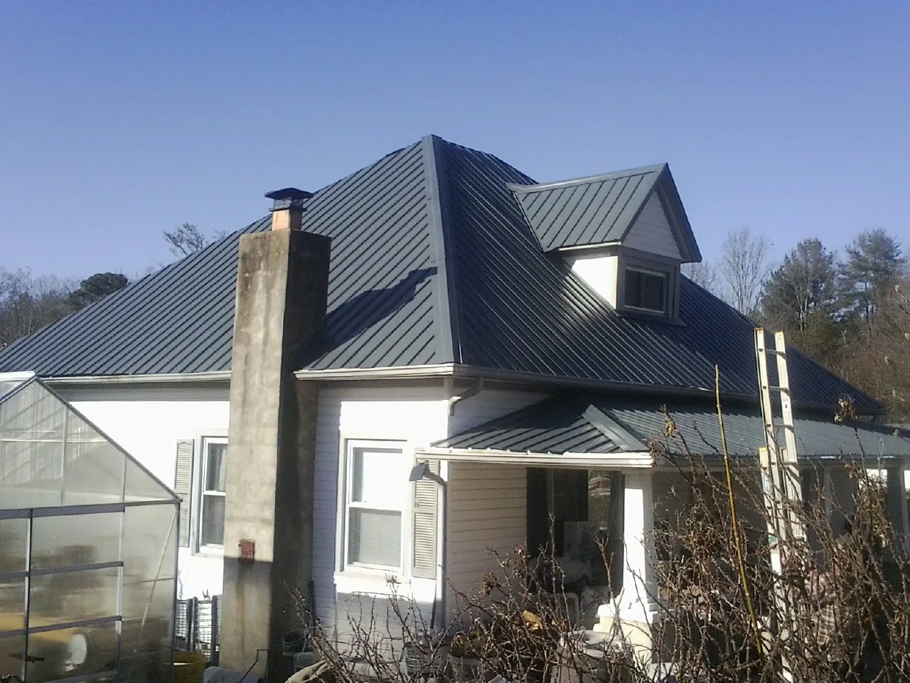 Dark blue standing seam metal roof on a white farmhouse with dormer — Slate & Tile Roof Repair by Roofing Brothers in Arab