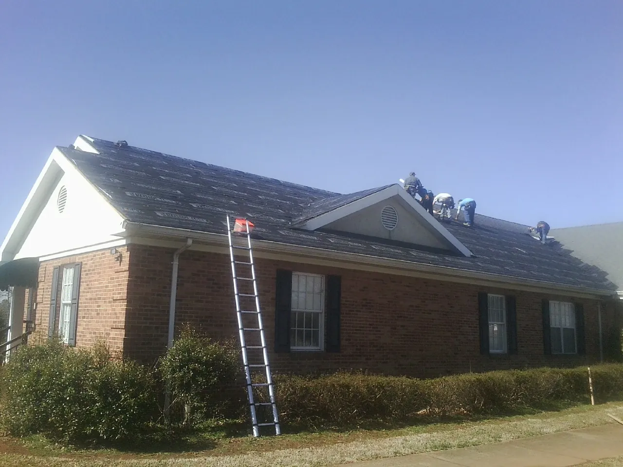 Crew tearing shingles off a brick ranch roof with a ladder set — Metal Roof Repair work by our crew in Arab