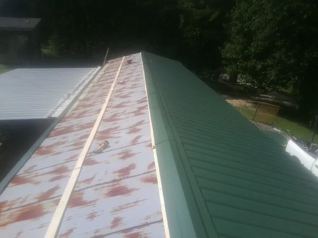 Old rusted panels beside newly installed green metal roofing — Wind Damage Roof Repair by Roofing Brothers in Arab