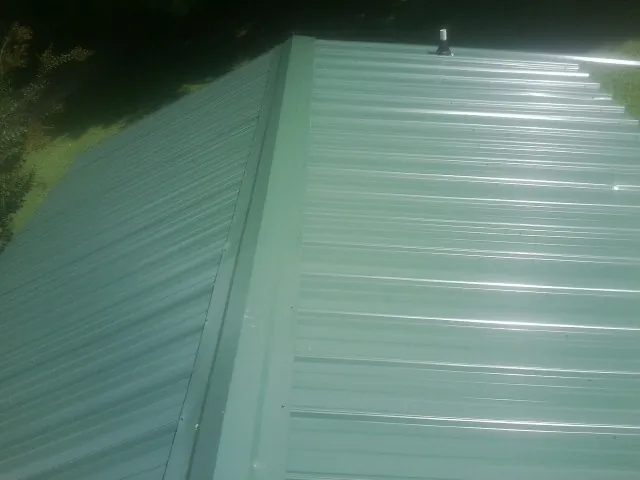 New green metal panels meeting at the ridge of a roof — Flat Roof Repair work by our crew in Arab