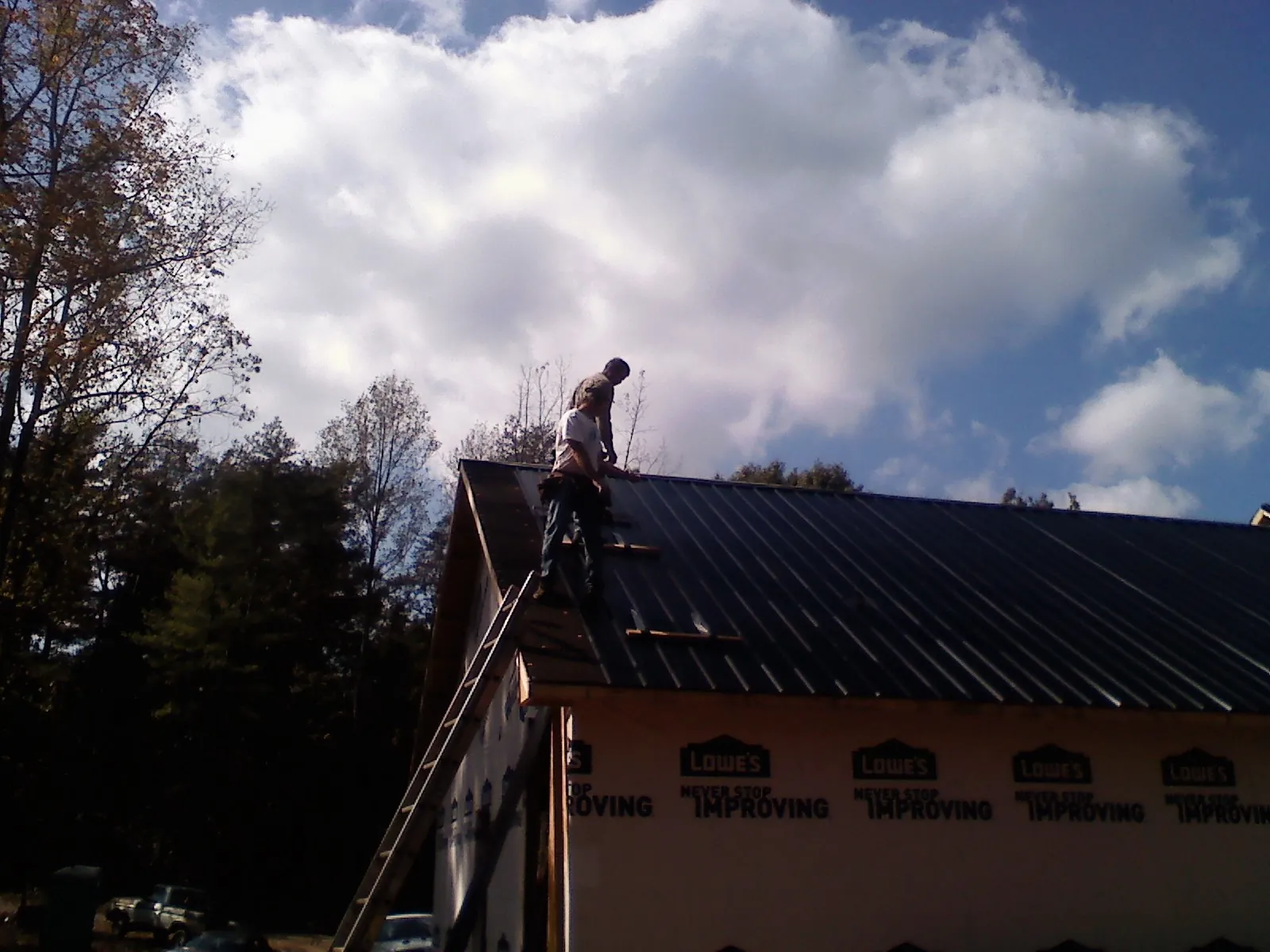 Roofer fastening dark metal panels high against a cloudy sky, from a Roof Inspection job in Arab